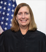 A smiling white woman with blonde hair wearing a judge's black robe.