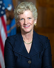 Portrait of Administrator Robin Carnahan. Robin has light hair and is wearing a blue suit standing next to the American flag.