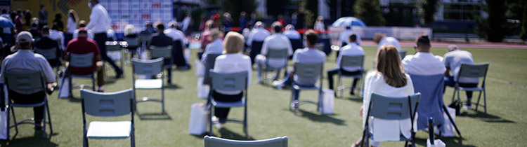 A view of chairs and seated people on a lawn, facing away from the camera