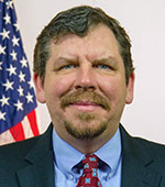 Headshot of Bob Stafford. Bob has short dark hair and is wearing a blue suit and red tie.
