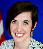 Headshot of Camille Tucker. Camille has short dark hair and is wearing a striped black and white suit.