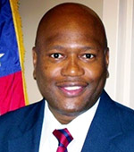 Portrait of Rob Miller, who has dark eyes and is wearing a blue jacket and a red and blue striped tie