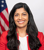 Portrait of Stephanie Joseph, who has long dark hair and is wearing a red jacket with a white shirt