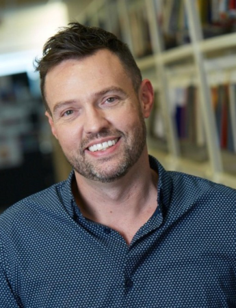 A person in a casual business shirt in front of a faded background.