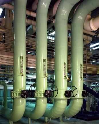 Four large green condenser supply pipes within a heating building