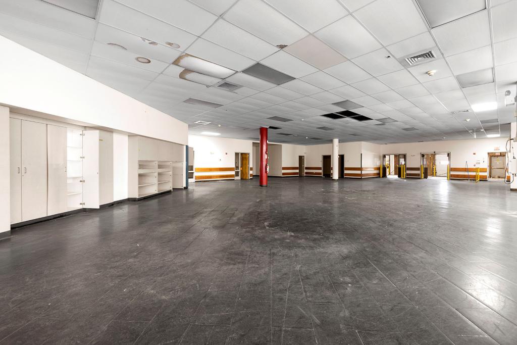 A large open office space with a red pillar, closets, shelves, a dark tiled floor, and seven doors.