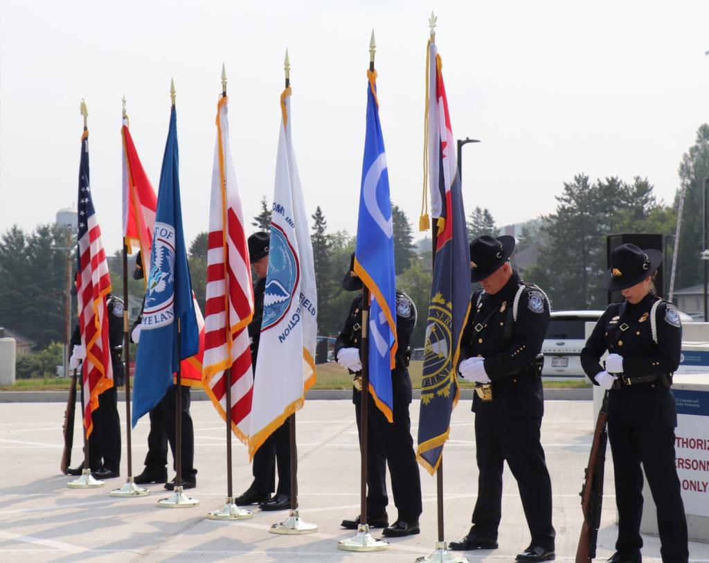 CBP officers stand behind the flags with their heads down