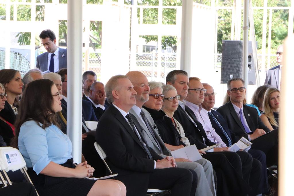 Many people are seated and looking out in the same direction while some people stand in the background