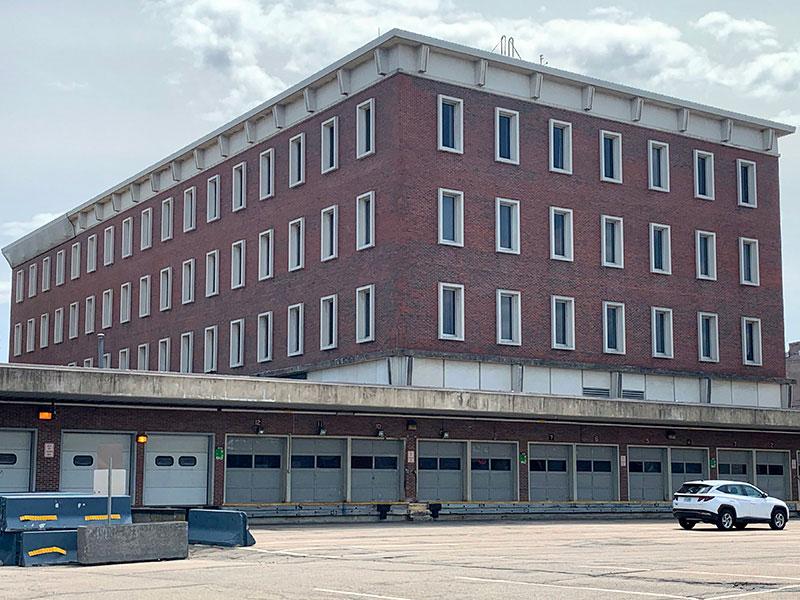 View of a 4-story brick building with a lengthy loading dock and multiple garage doors