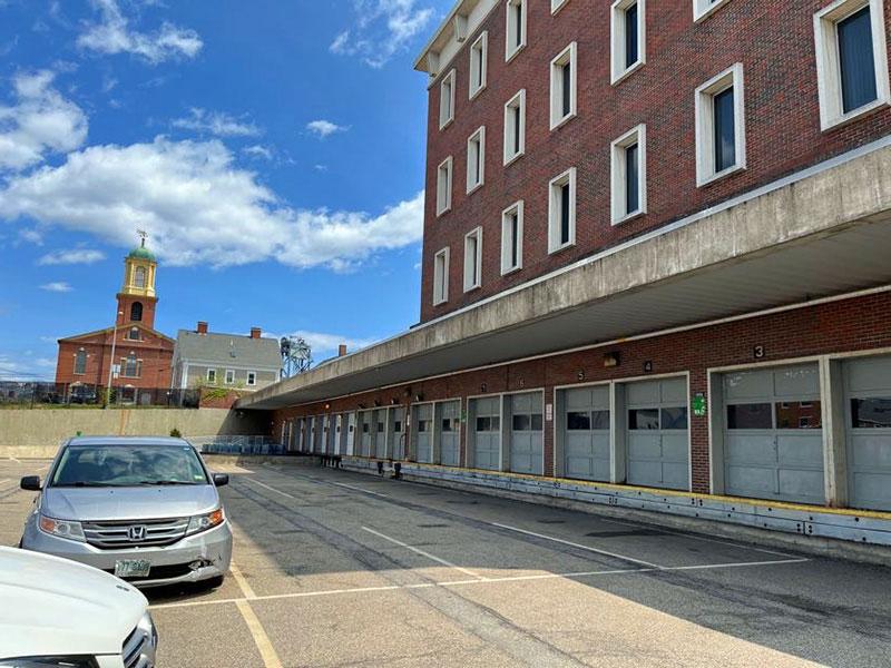 View of a parking lots next to a 4-story brick building with multiple garage doors.