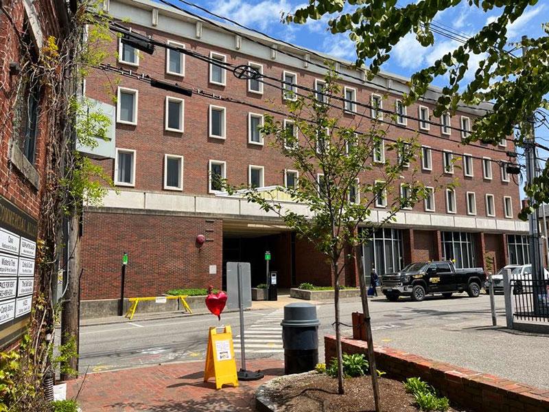 View of the side of a 4-story red brick building, a sidewalk, and a crosswalk.