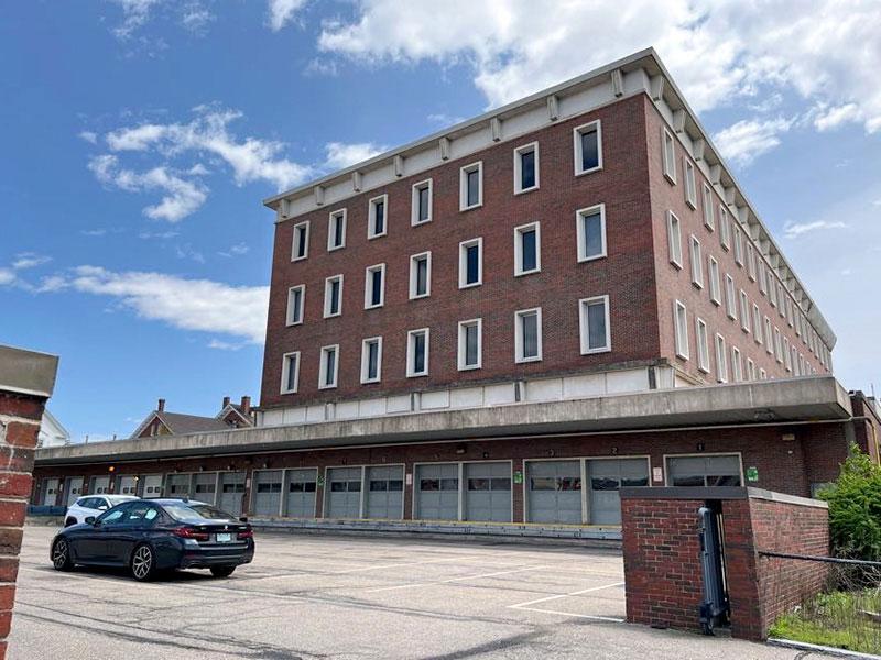 Side view of a 4-story red-brick building, garage doors, and parking lot.