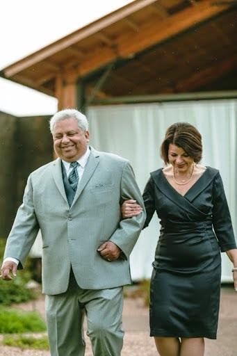 A man holds a woman's hand wearing formal dress outdoors and walking.