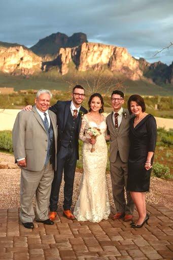 Three men wearing suits stand with a bride in the center and another woman wearing a dress on the right.