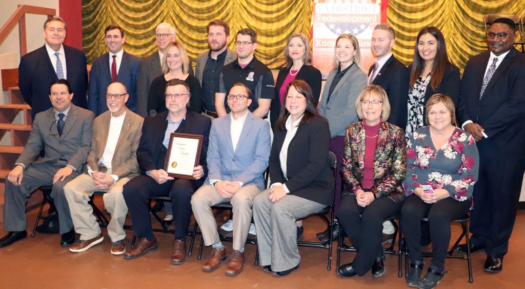 Eleven people stand behind a row of seven people seated for a group photo