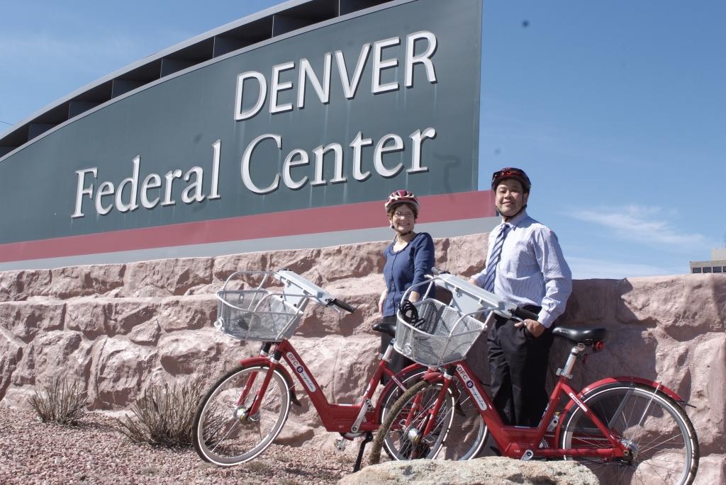 Two people with bicycles stand in front of the DFC sign.