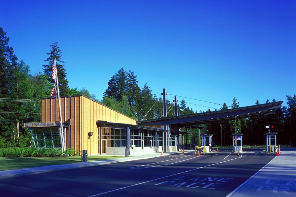 Port Roberts U.S. Border Station, with a small gold 2-level building with a 3-lane canopy and booths in front of it, and a clear blue sky