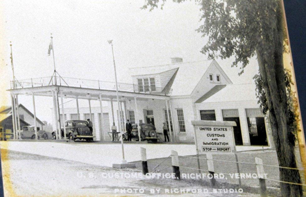 Historic photo showing the front entrance of the building with two cars parked under the portico.